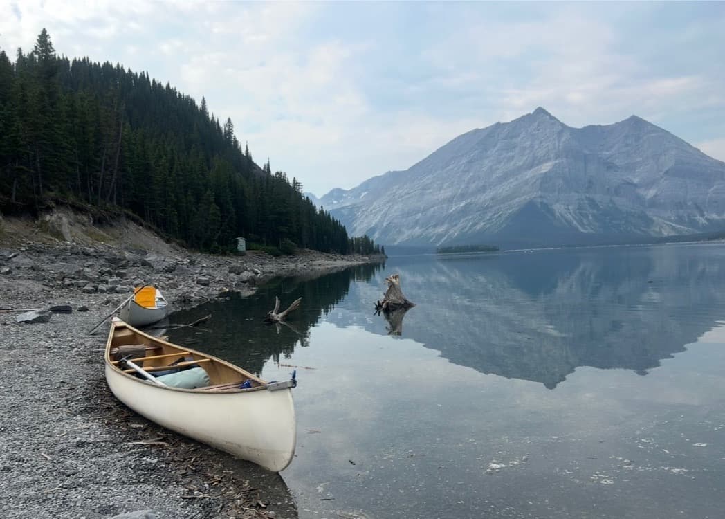 Canoe resting on the shore of a still alpine lake, the Canadian Rockies reflected on its surface